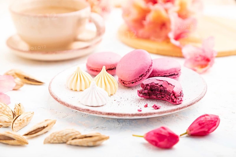Purple macarons or macaroons cakes with cup of coffee on a white concrete background decorated with flowers. Side view, close up, selective focus