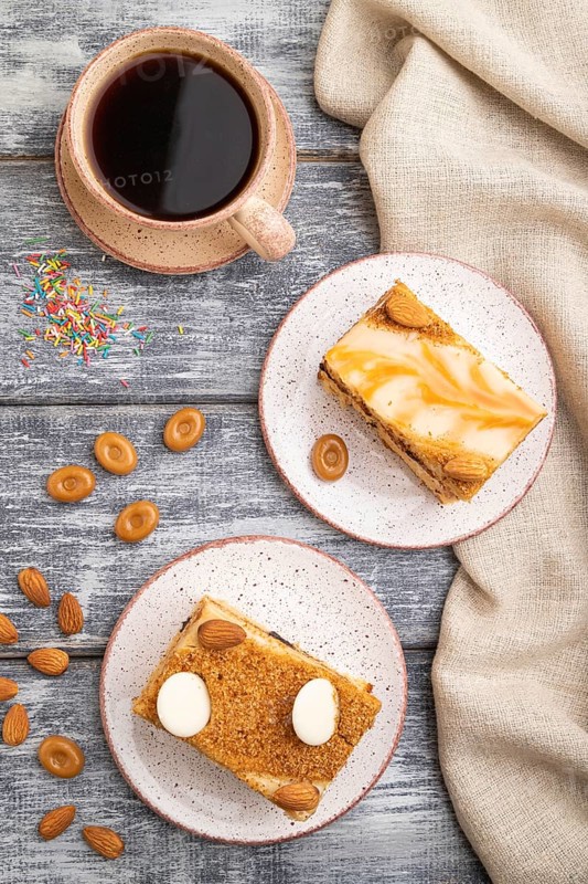 Honey cake with milk cream, caramel, almonds and a cup of coffee on a gray wooden background and linen textile. Top view, flat lay, close up