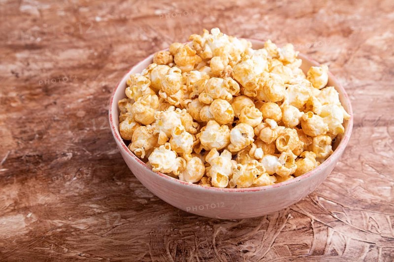 Popcorn with caramel in ceramic bowl on brown concrete background. Side view, close up
