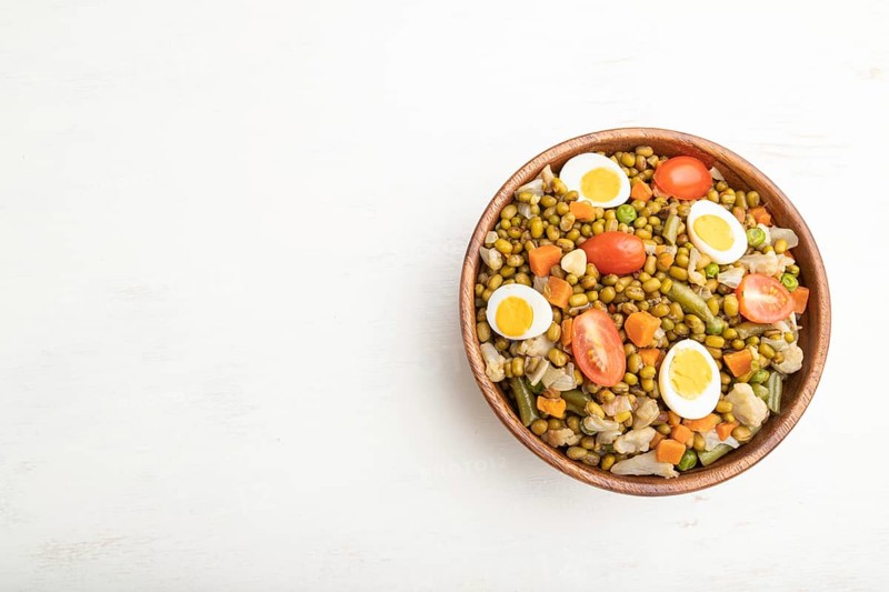Mung bean porridge with quail eggs, tomatoes and microgreen sprouts on a white wooden background. Top view, flat lay, copy space