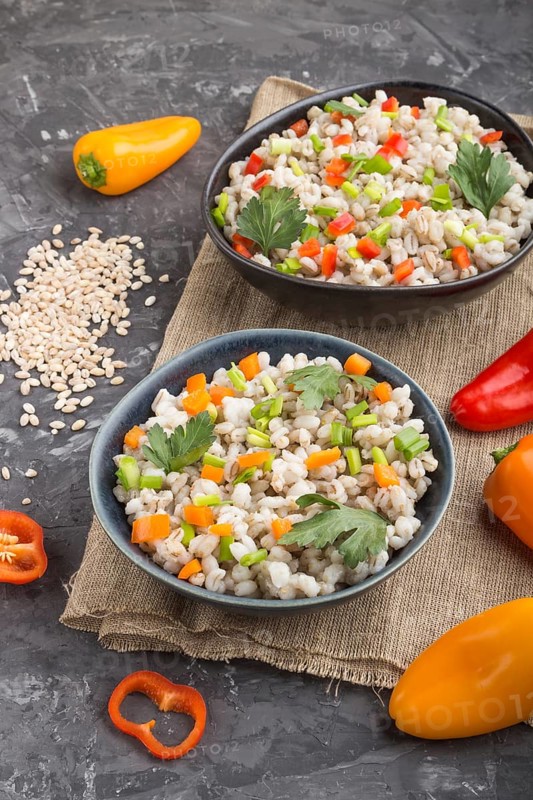 Pearl barley porridge with vegetables in blue ceramic bowls on a black concrete background and linen textile. Side view, close up. Russian traditional cuisine