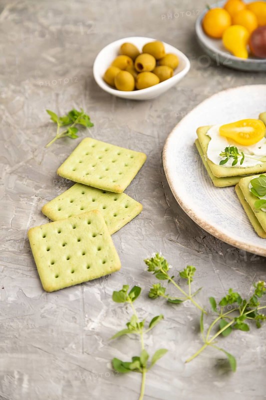 Green cracker sandwiches with cream cheese and cherry tomatoes on gray concrete background. side view, close up, selective focus