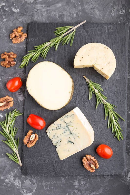 Blue cheese and various types of cheese with rosemary and tomatoes on black slate board on a black concrete background. Top view, close up, flat lay