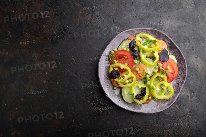Vegetarian salad from green pea, tomatoes, pepper and basil on a black concrete background. top view, copy space, flat lay