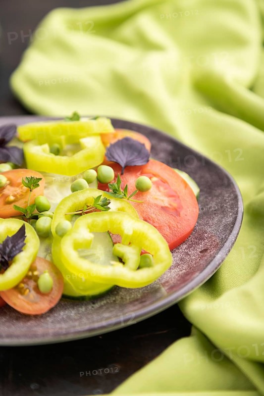 Vegetarian salad from green pea, tomatoes, pepper and basil on a black concrete background and green textile. Side view, close up, selective focus