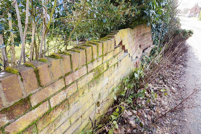 Impact damage to red brick garden wall caused by vehicle reversing, Suffolk, England, UK