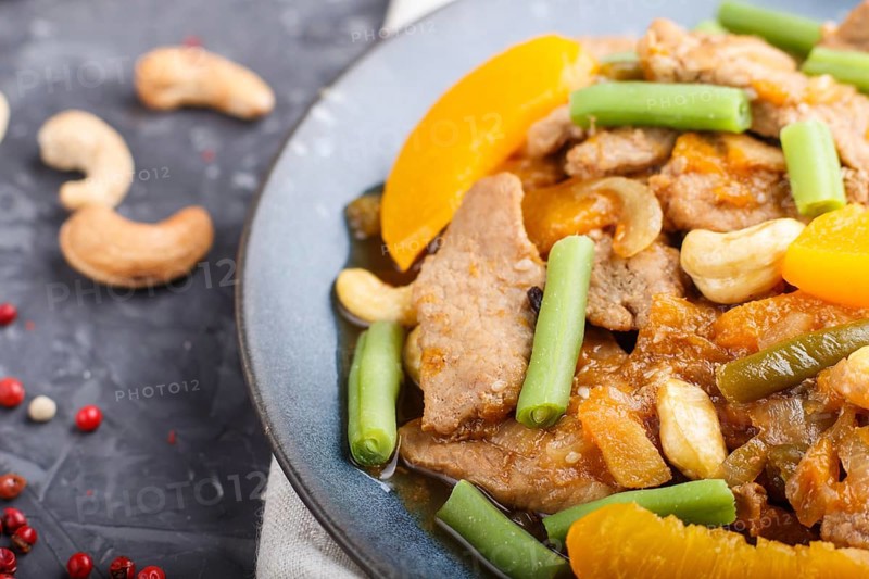 Fried pork with peaches, cashew and green beans on a black concrete background. Top view, close up, chinese cuisine, selective focus, macro