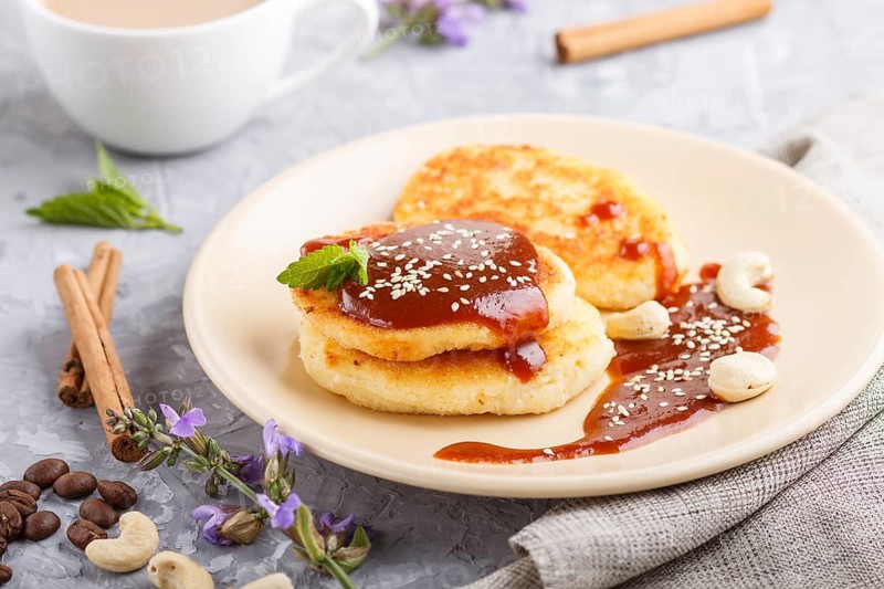 Cheese pancakes with caramel sauce on a beige ceramic plate and a cup of coffee on a gray concrete background. side view, close up