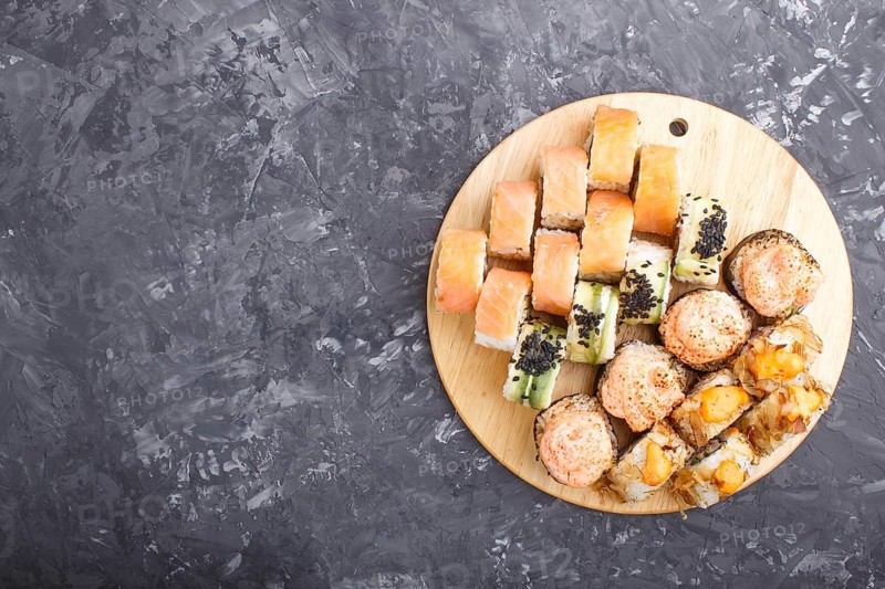 Mixed japanese maki sushi rolls set on black concrete background. Top view, copy space, flat lay