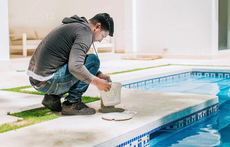 Worker removing trash from swimming pool filter basket. Man cleaning swimming pool garbage filter