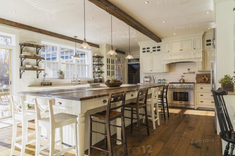 White painted maple wood antique style cabinets with tan coloured quartz countertops, island with brown stained wood plank countertop and high back bar stools in kitchen with stained oak wood floorboards inside country style home, Quebec, Canada, North America