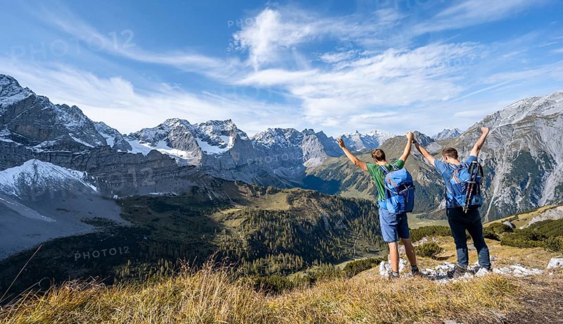 Two mountaineers hand in hand with outstretched arms, on a hiking trail, mountain panorama with rocky steep peaks, view of summit Laliderspitze, Dreizinkenspitze and Spritzkarspitze, hike to the summit of Hahnkampl, Engtal, Karwendel, Tyrol, Austria, Europe