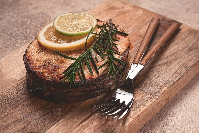 Salmon steak, fried, on a cutting board, top view, rosemary, lemon and lime, homemade, one serving, no people