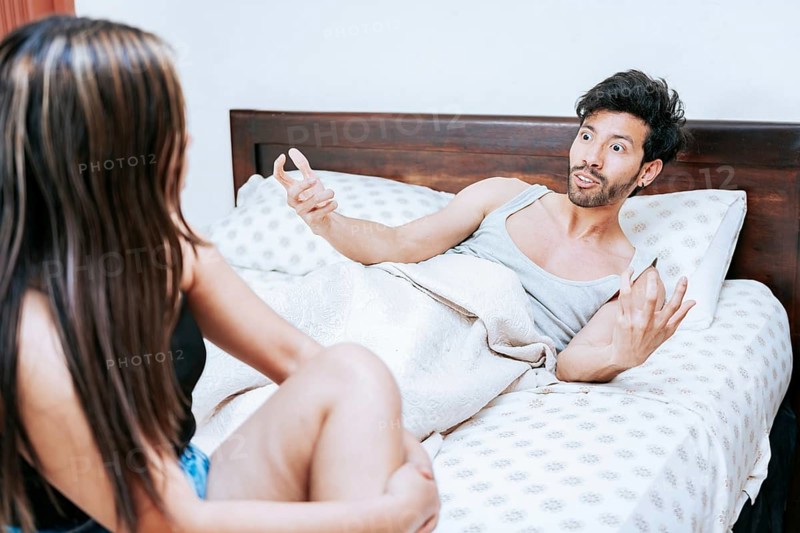 Young couple screaming at each other in bed. Husband arguing with his wife in bed. Upset woman with husband sitting on bed