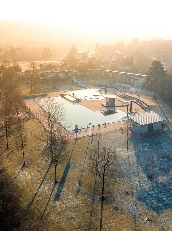 The morning sun casts long shadows over a swimming pool with frost-covered grass and trees, ENCW outdoor pool Calw, Stammheim, Black Forest, Germany, Europe