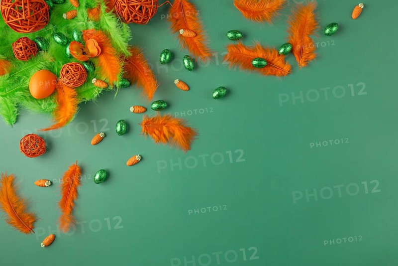 Decorative arrangement with feathers and chocolate eggs in green and orange on a green surface