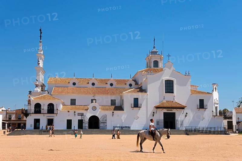 Ein großes weißes Gebäude mit einem Reiter auf einem sandigen Platz und mehreren Menschen im Vordergrund, Wallfahrtsort, El Rocío, Rocío, Rocio, Huelva, Andalusien, Spanien