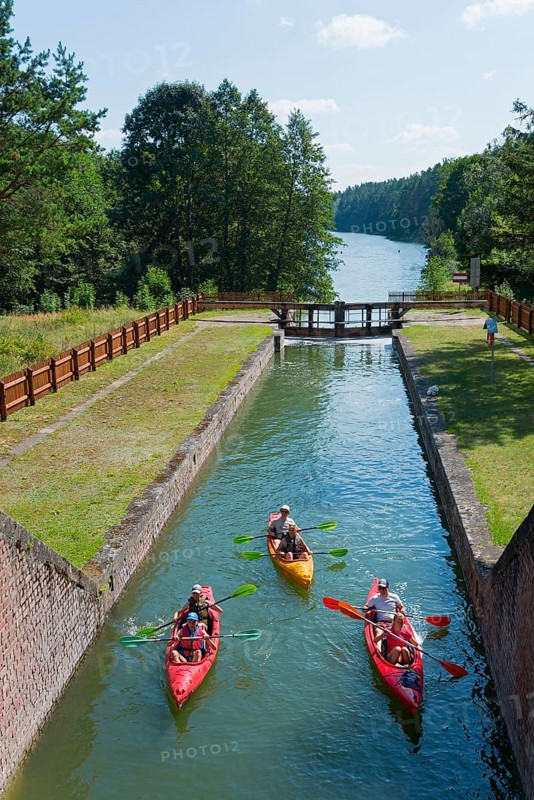 Three kayaks travelling through a narrow forest channel under a clear sky in nature, Sluza Paniewo, lock between the lakes Paniewo and Krzywe, Plaska, Powiat Augustowski, Podlaskie Voivodeship, Poland, Europe