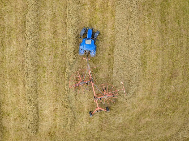 An aerial view shows a tractor with a hay tedder ploughing patterns into a hay field, Dachtel. Black Forest, Germany, Europe
