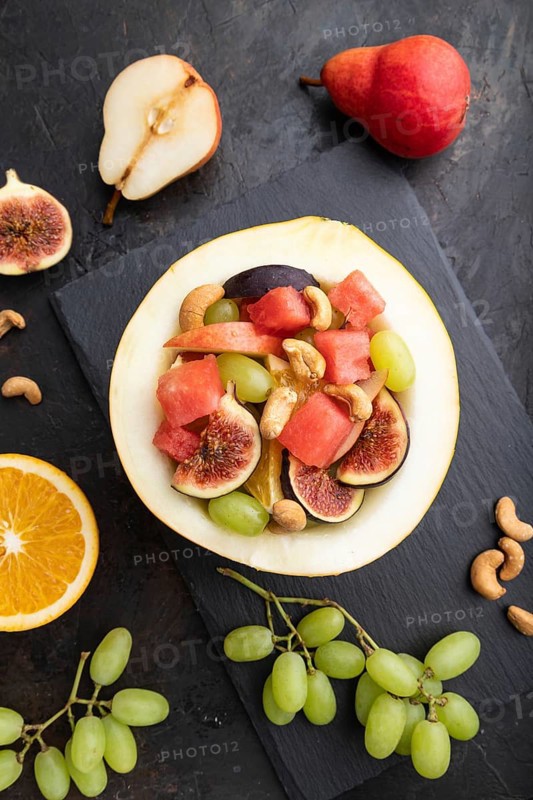 Vegetarian fruit salad of watermelon, grapes, figs, pear, orange, cashew on slate board on a black concrete background. Top view, flat lay, close up