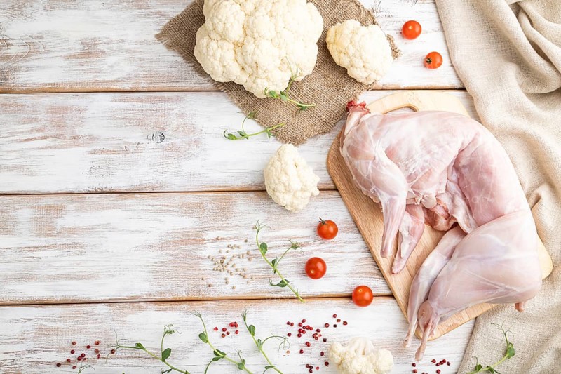 Whole raw rabbit with cauliflower, tomatoes and spices on a white wooden background and linen textile. Top view, flat lay, copy space