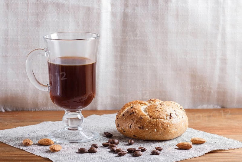 Glass cup of coffee with bun on a wooden background and linen textile. close up, copy space