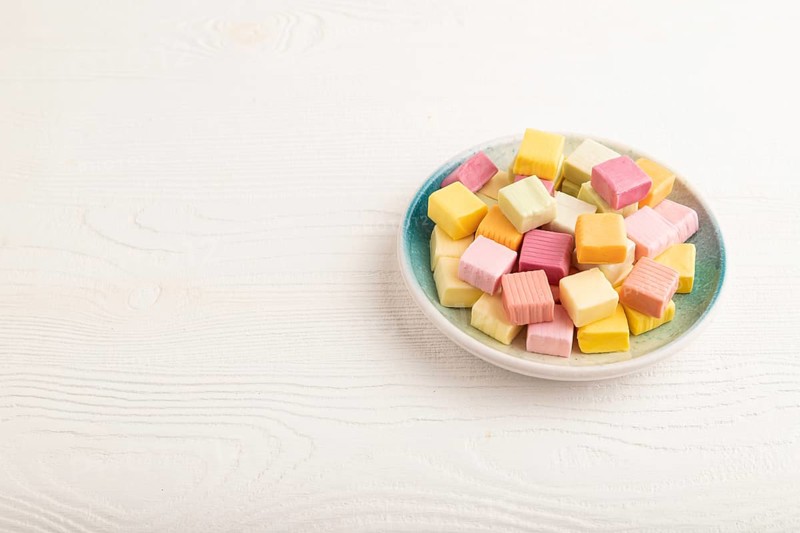 Various fruit jelly chewing candies on plate on white wooden background. apple, banana, tangerine, kiwi, side view, copy space