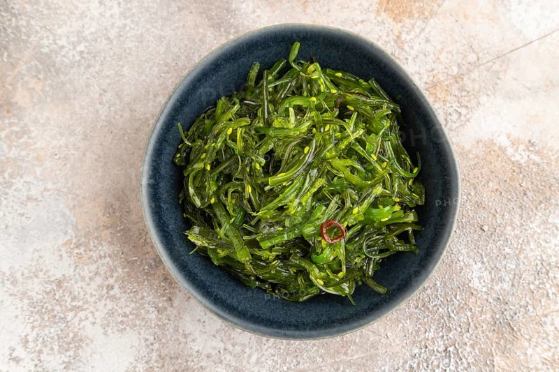 Chuka seaweed salad in blue ceramic bowl on brown concrete background. Top view, flat lay