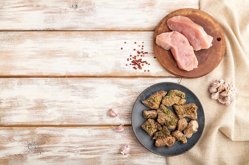 Stewed turkey fillet with garlic on white wooden background and linen textile. Top view, flat lay, copy space