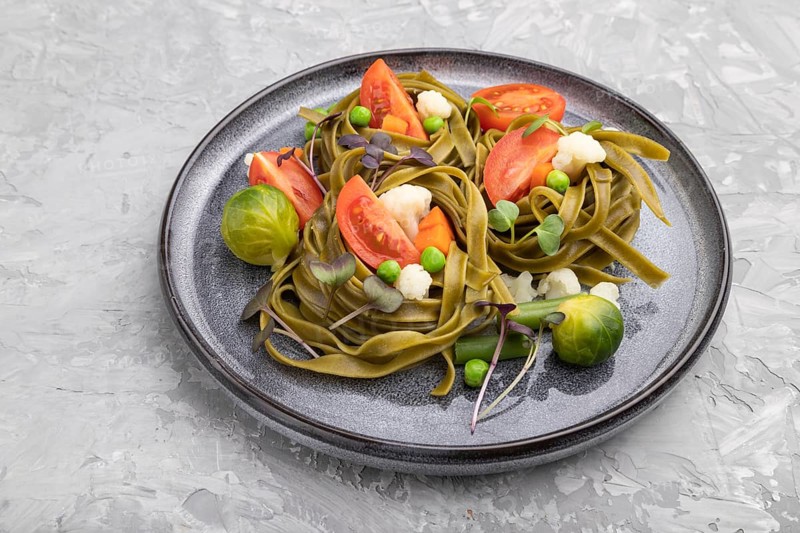 Tagliatelle green spinach pasta with tomato, pea and microgreen sprouts on a gray concrete background. Side view, close up