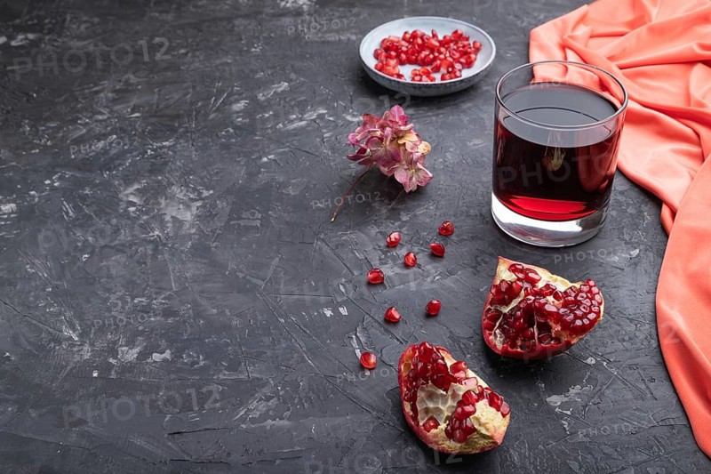 Glass of pomegranate juice on a black concrete background with red textile. Side view, close up, copy space