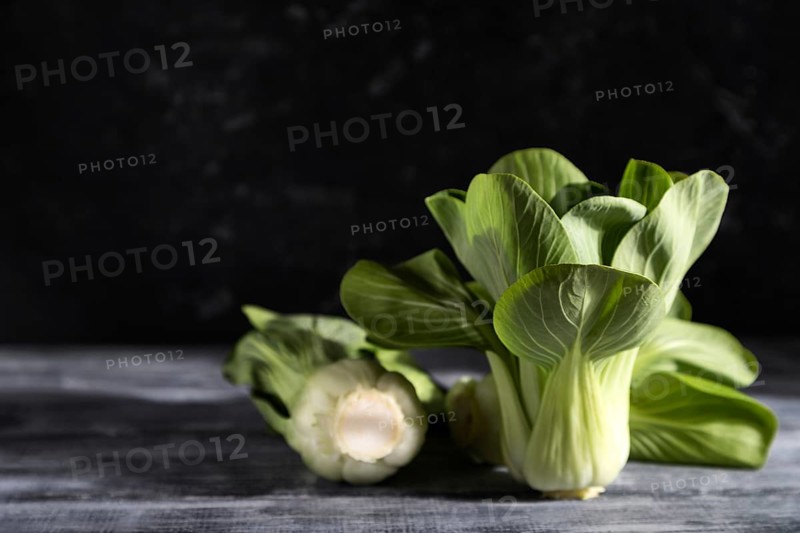Fresh green bok choy or pac choi chinese cabbage on a gray wooden background. Hard light, contrast, dark, moody. Side view, copy space, selective focus