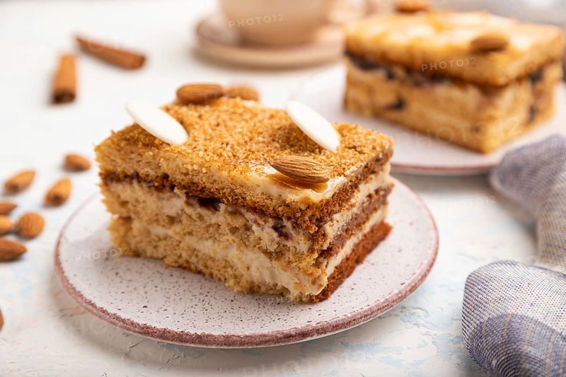 Honey cake with milk cream, caramel, almonds and a cup of coffee on a white concrete background and linen textile. Side view, selective focus, close up