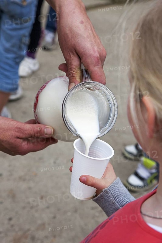 Farmer pouring fresh milk in little girl's plastic cup at farm