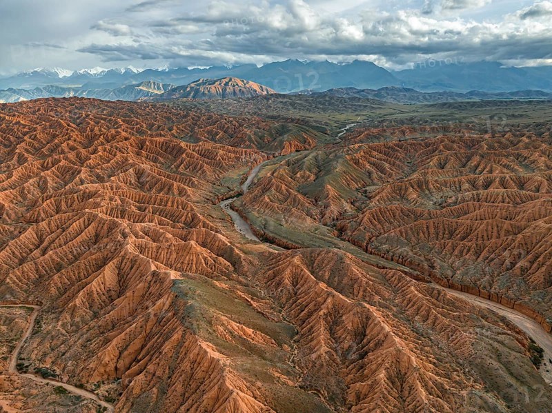 River bed runs through a landscape of eroded hills, badlands at sunset, mountain peaks of the Tian Shan Mountains in the background, aerial view, Canyon of the Forgotten Rivers, Issyk Kul, Kyrgyzstan, Asia