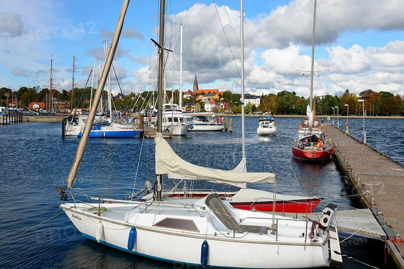 Sailboats lying in the calm waters of a marina, with a city view and cloudy sky in the background, Eckernförde, Schleswig-Holstein, Germany, Europe
