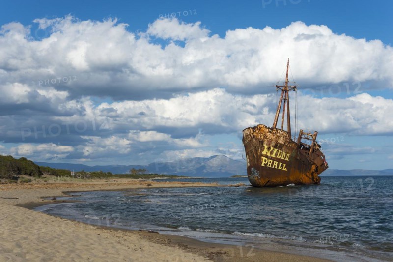 A rust-coloured shipwreck protrudes from a calm stretch of sea under a cloudy sky, Dimitrios shipwreck, Glyfada beach, Selinitsa, Gythio, Githio, Gythion, Mani, Laconia, Peloponnese, Greece, Europe
