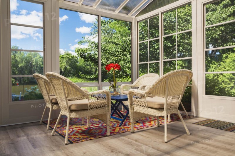 Beige wicker armchairs and blue wooden table in sunroom at back of luxurious residential home, Quebec, Canada, North America