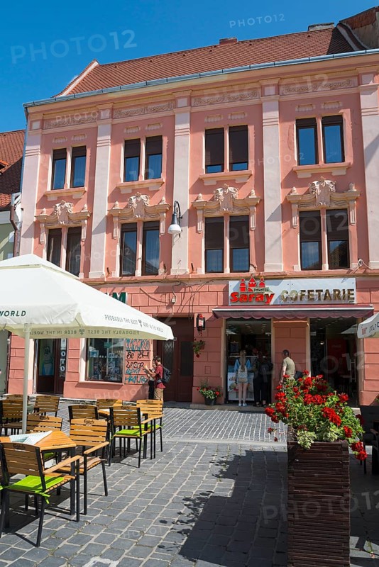 Street view of a pink façade with elaborate stucco details and a café in the foreground, town house in the historic centre, Brasov, Brasov, Transylvania, Romania, Europe