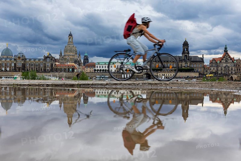 The Dresden silhouette with a cyclist and dark clouds behind the Church of Our Lady is reflected in a puddle on the Elbe cycle path, Elbe cycle path, Dresden, Saxony, Germany, Europe