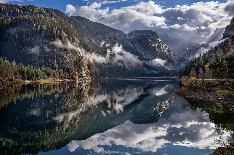 The Vordere Gosausee in autumn. In the background, the Dachstein mountain range in clouds. Partly blue sky and sun. Forest covered in clouds. Individual rays of sunshine. Vorderer Gosausee, Gosau, Gosau Valley, Salzkammergut, Upper Austria, Austria, Europe