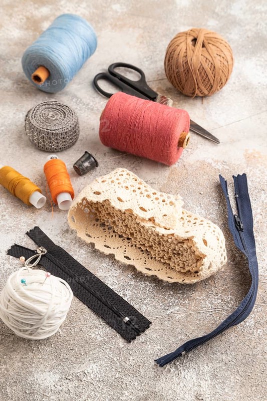 Sewing accessories: scissors, thread, thimbles, braid on brown concrete background. Side view, close up