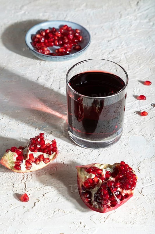 Glass of pomegranate juice on a white concrete background. Hard light, contrast. Side view, close up