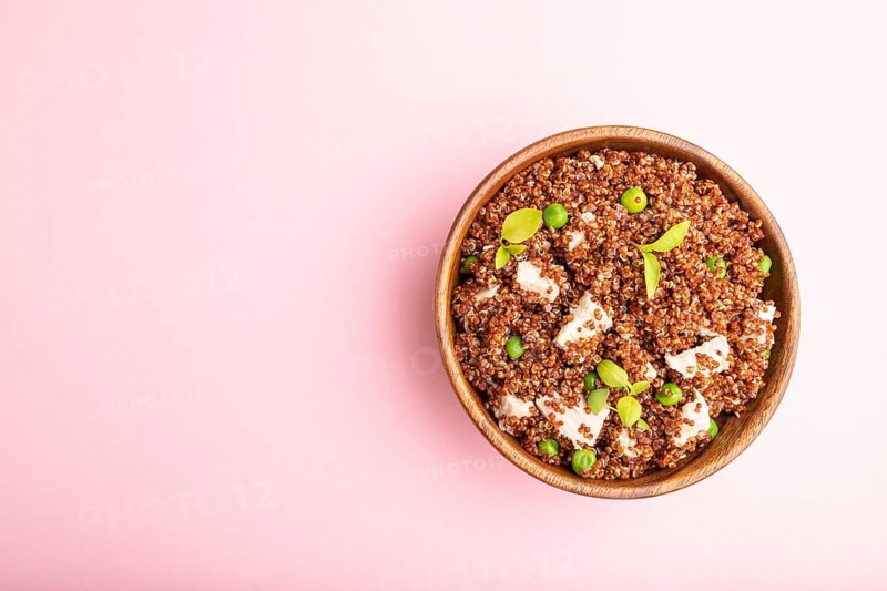 Quinoa porridge with green pea and chicken in wooden bowl on a pastel pink background. Top view, flat lay, copy space