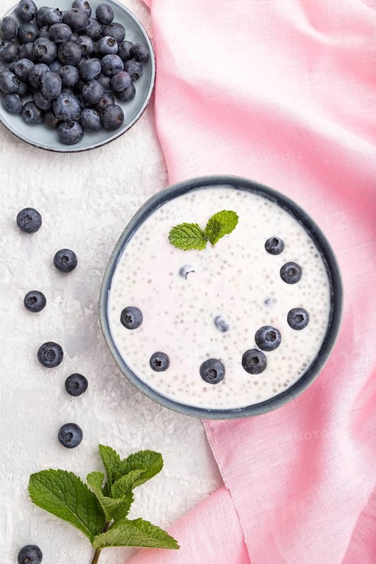 Yogurt with blueberry in ceramic bowl on gray concrete background and pink linen textile. top view, flat lay, close up