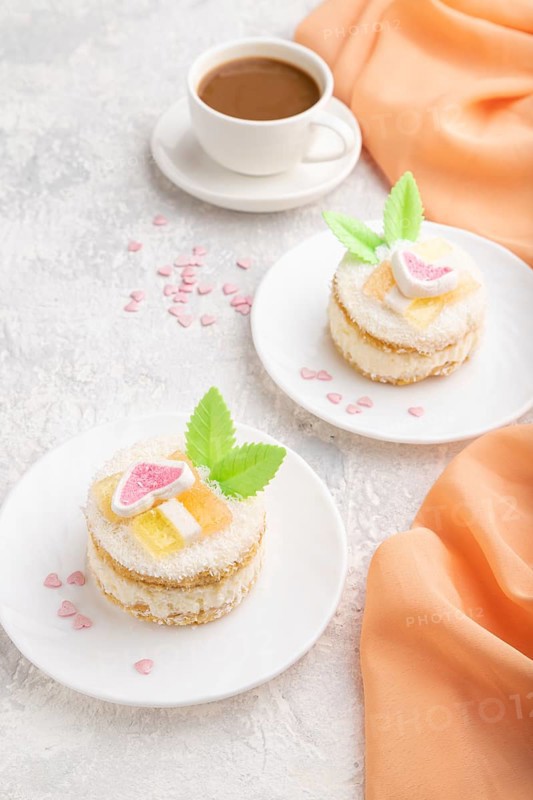 Decorated cake with milk and coconut cream with cup of coffee on a gray concrete background and orange textile. Side view, close up