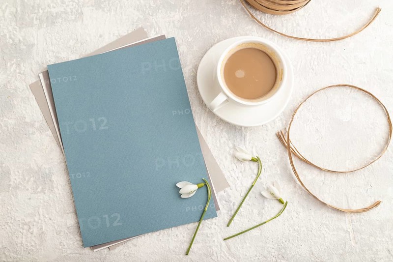 Blue paper sheet mockup with spring snowdrop galanthus flowers and cup of coffee on gray concrete background. Blank, business card, top view, flat lay, close up, still life. spring concept