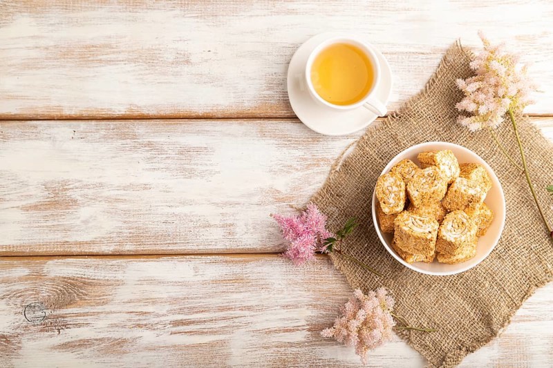 Traditional turkish delight (rahat lokum) in white ceramic plate with cup of green tea on a white wooden background. top view, flat lay, copy space