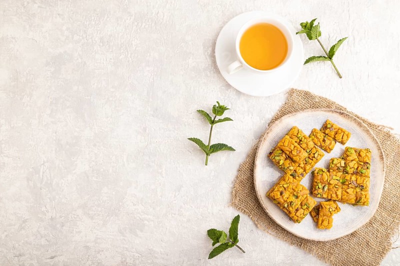 Traditional iranian dessert sohan with cup of green tea on a gray concrete background and linen textile. top view, flat lay, copy space