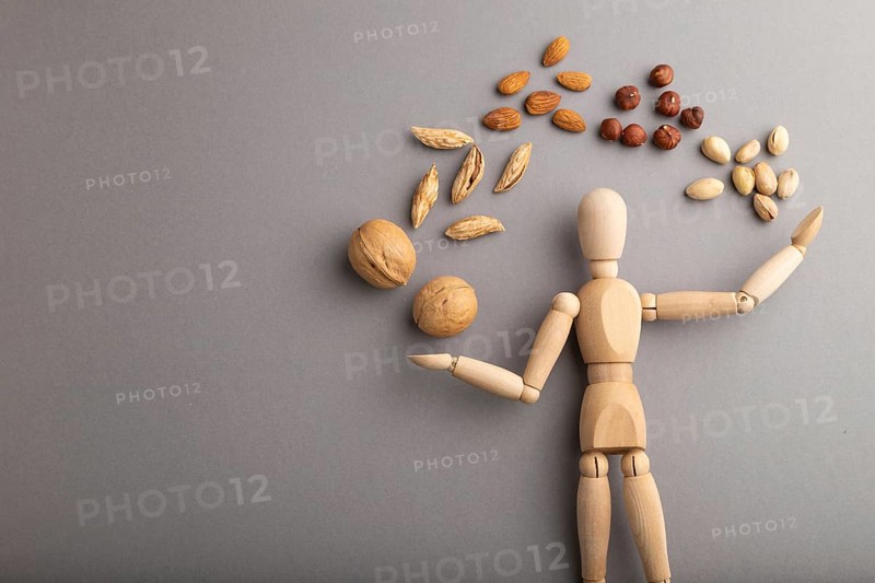 Wooden mannequin juggling nuts on gray pastel background. close up, isolated, delivery concept, copy space